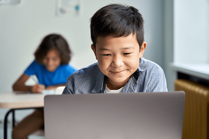 a young boy using a laptop in a classroom