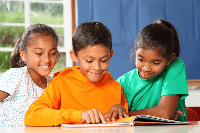 elementary ages students reading a book together at a desk