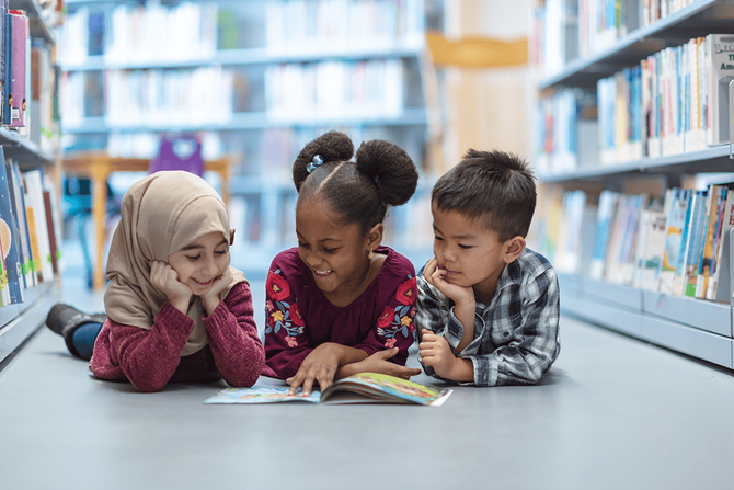 elementary ages students reading a book together on the floor of the library