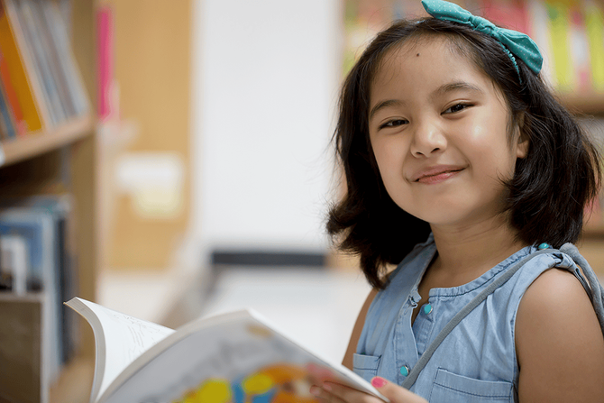 girl with a book smiling at the camera